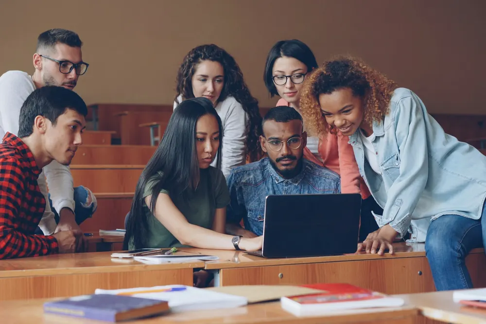 Students gathered around a laptop in a lecture hall