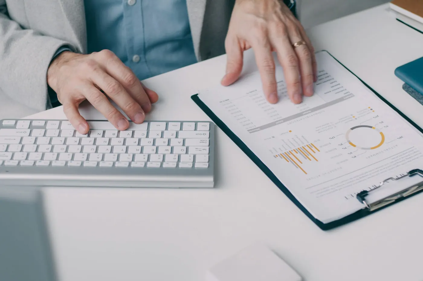 Hands typing on a keyboard beside a clipboard of printed reports